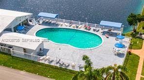 1000 SW 11 Avenue, #12, Hallandale Beach, Hallandale Beach, FL 33009 In-ground swimming pool featuring a concrete surround, white perimeter fencing, and dual shade structures