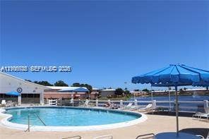1000 SW 11 Avenue, #12, Hallandale Beach, Hallandale Beach, FL 33009 Outdoor swimming pool featuring a curved concrete deck and a white perimeter fence overlooking a water feature