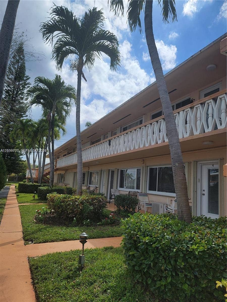 1000 SW 11 Avenue, #12, Hallandale Beach, Hallandale Beach, FL 33009 Two-story stucco building exterior featuring a geometric patterned balcony railing, mature palm trees, landscaped shrubbery, and paved pedestrian walkways