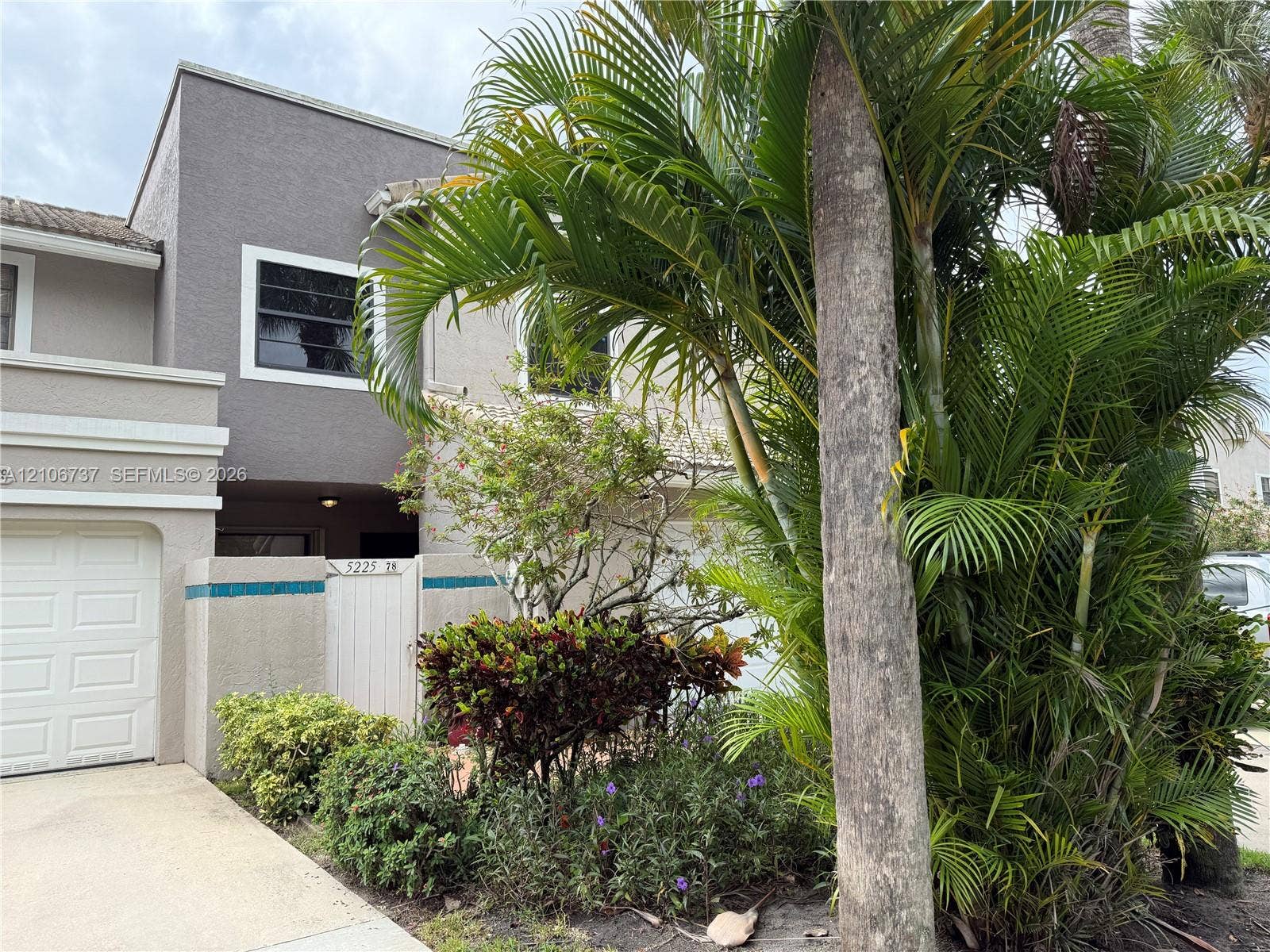 5225 Monterey Circle, #G, Delray Beach, FL 33484 Two-story stucco exterior featuring a concrete tile roof, attached single-car garage, and gated courtyard entry accented with decorative tile trim
