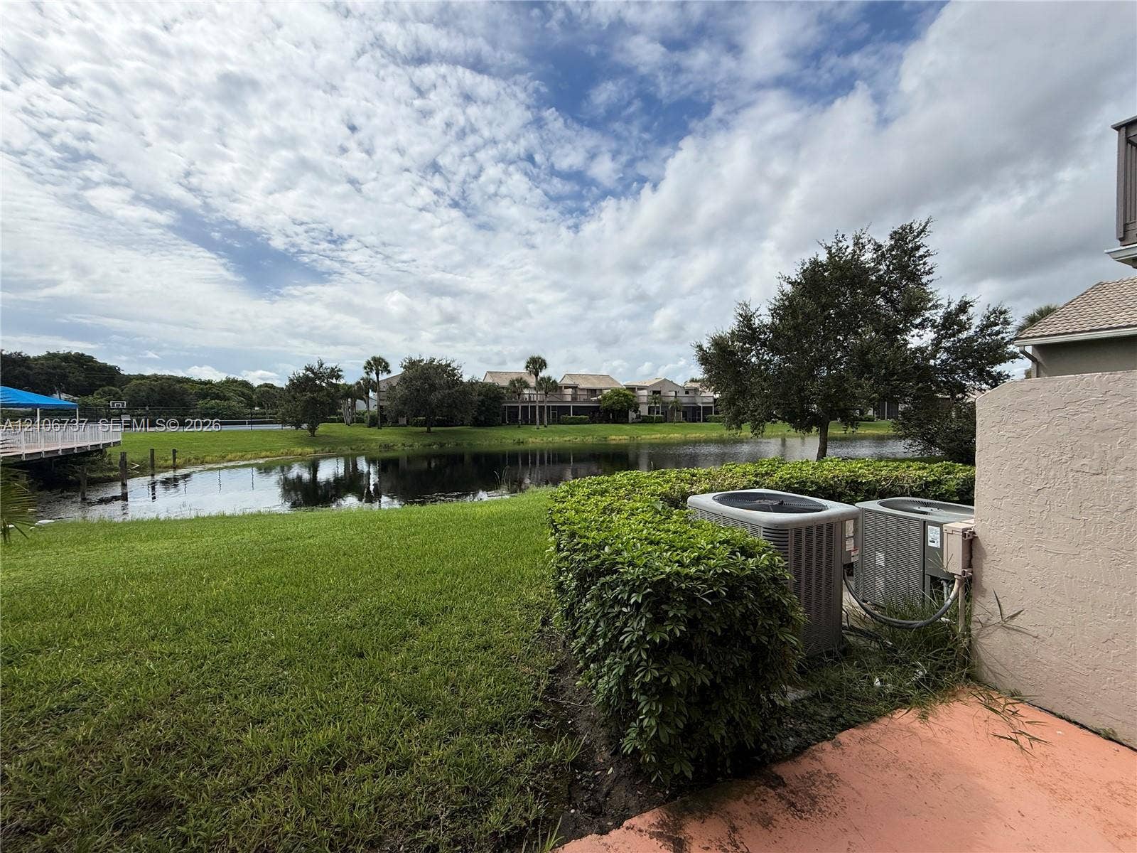 5225 Monterey Circle, #G, Delray Beach, FL 33484 Waterfront property featuring a pond, manicured lawn, hedge landscaping, and exterior HVAC units