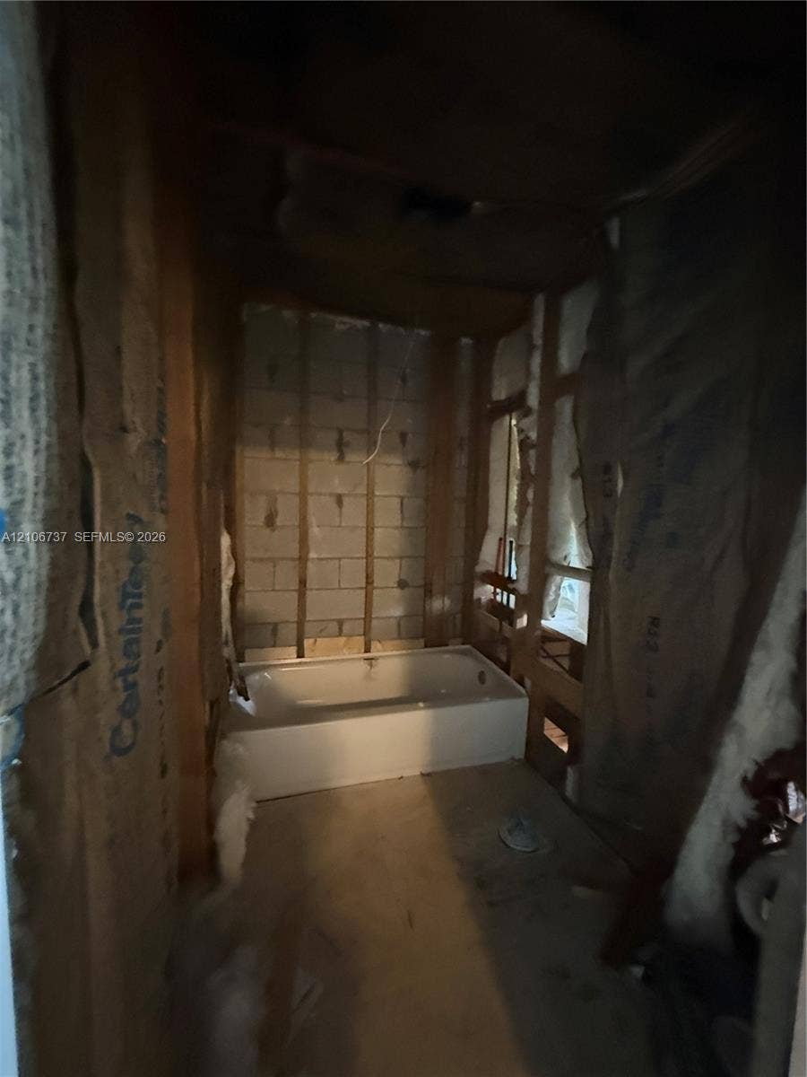 5225 Monterey Circle, #G, Delray Beach, FL 33484 White rectangular bathtub set within an unfinished space featuring exposed concrete block walls, wood stud framing, and fiberglass insulation