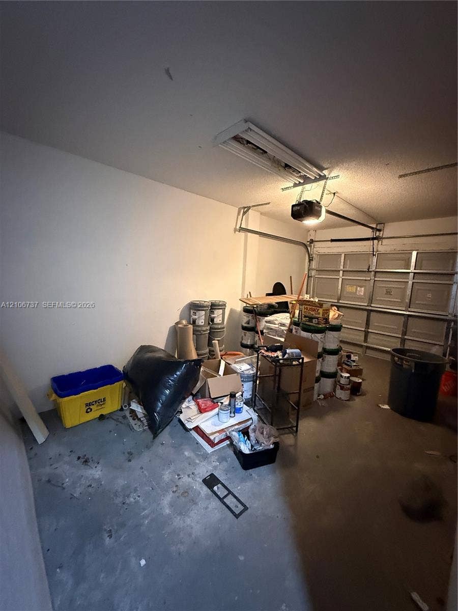 5225 Monterey Circle, #G, Delray Beach, FL 33484 Enclosed garage featuring a metal paneled sectional door, concrete flooring, and overhead lighting