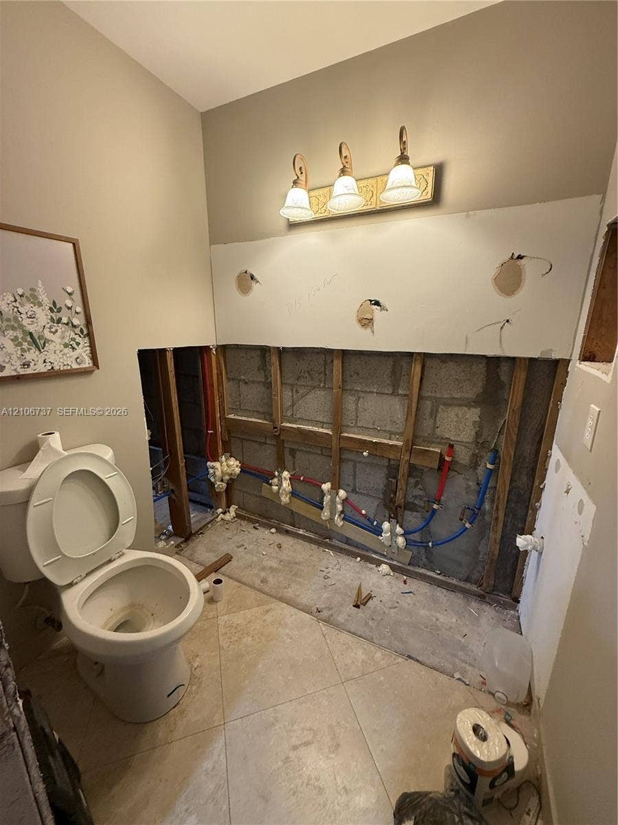 5225 Monterey Circle, #G, Delray Beach, FL 33484 Ceramic tile flooring, three-light wall-mounted vanity fixture, and exposed masonry wall with accessible plumbing infrastructure