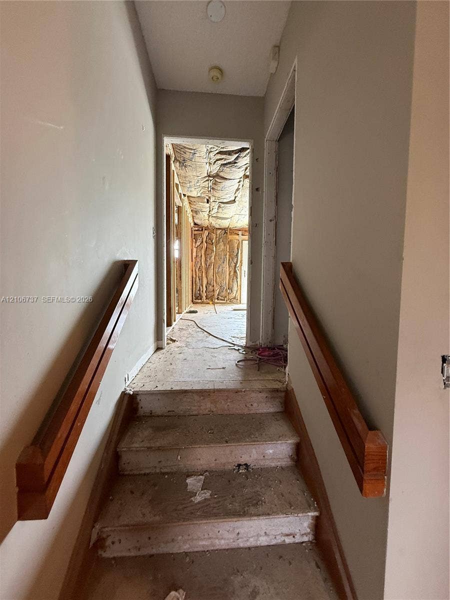 5225 Monterey Circle, #G, Delray Beach, FL 33484 Stairway featuring wood-finish handrails on both sides, leading to an interior space with exposed wall studs and unfinished insulation