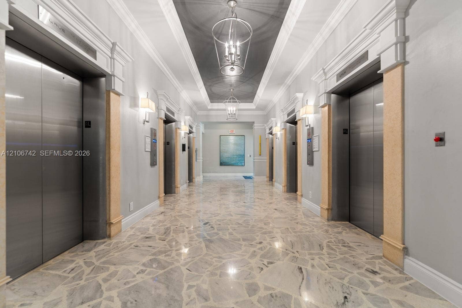 Elevator lobby featuring polished stone flooring, stainless steel elevator doors, crown molding, tiered metal pendant lighting, and decorative pilasters