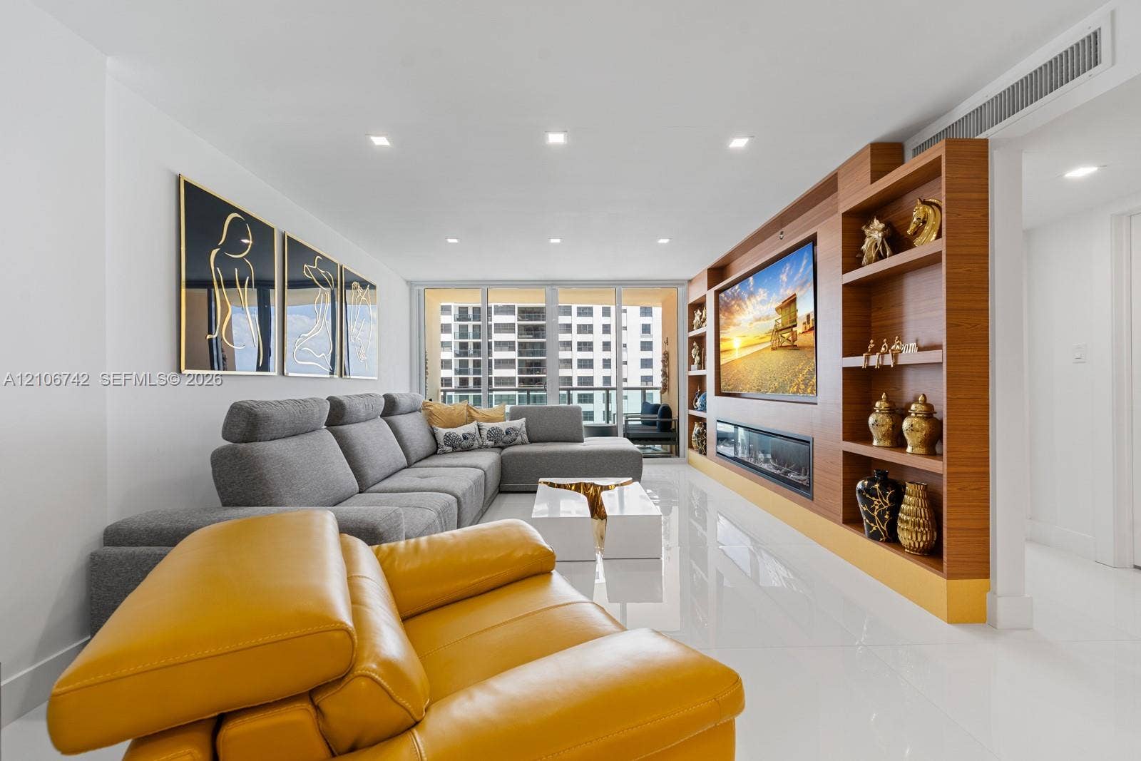 Living area featuring white polished flooring, recessed lighting, floor-to-ceiling glass sliding doors, and a custom built-in wood-finish wall unit with an integrated fireplace