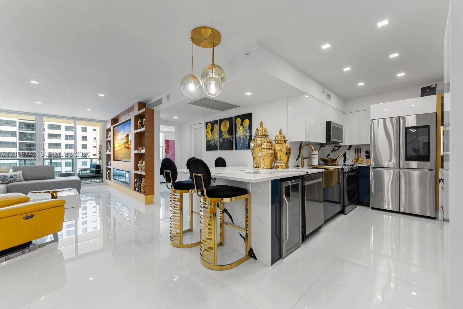 Open-concept kitchen featuring high-gloss cabinetry, a central waterfall-edge island, stainless steel appliances, and integrated beverage refrigeration