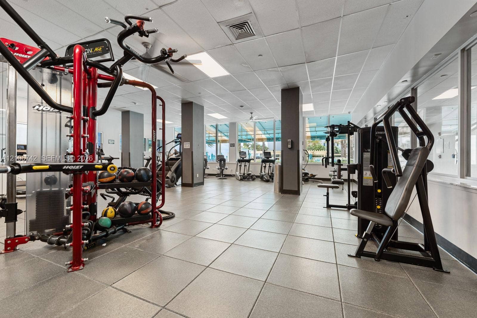 Fitness center featuring tile flooring, drop ceiling with recessed lighting, structural support pillars, and floor-to-ceiling windows