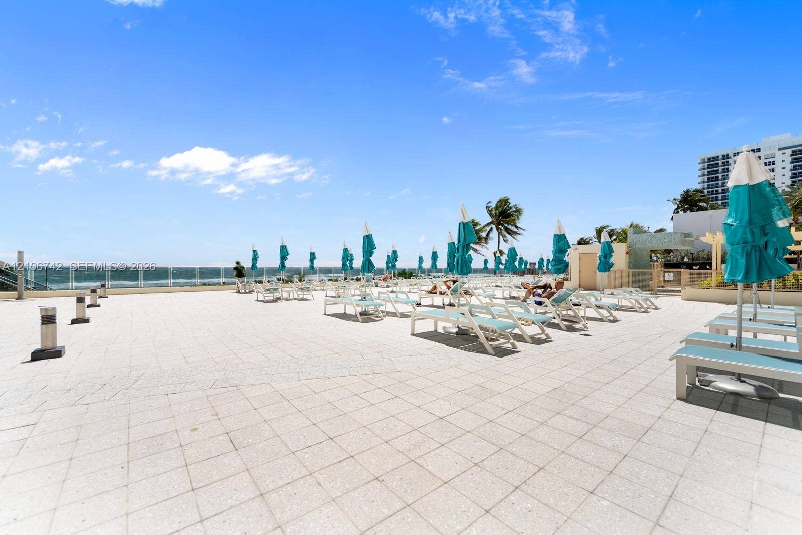 Expansive paved terrace featuring a glass panel railing, ocean backdrop, and integrated low-profile lighting fixtures
