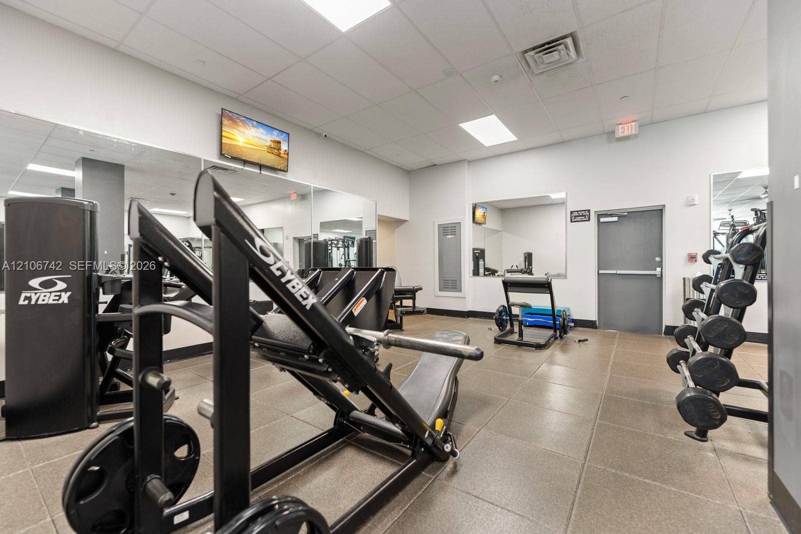 Fitness center featuring ceramic tile flooring, full-wall mirrors, recessed lighting, and integrated wall-mounted television