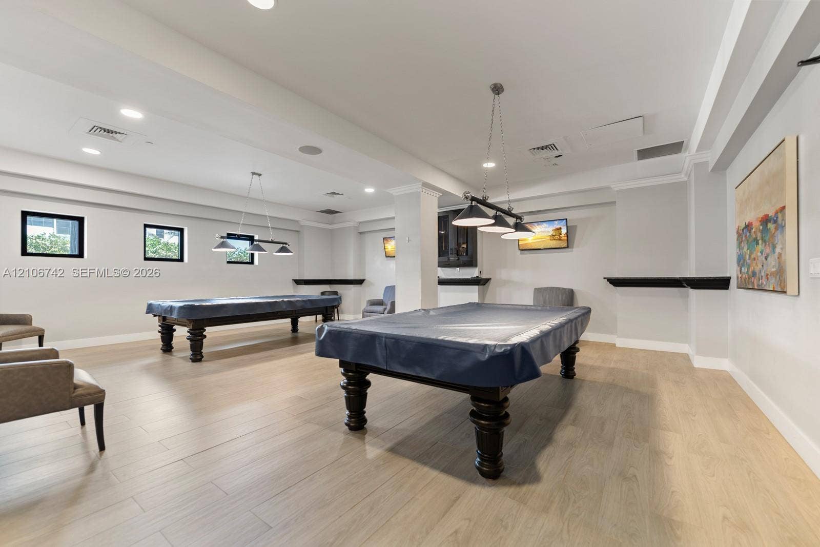 Spacious interior featuring wood-finish flooring, recessed lighting, crown molding, multi-light pendant fixtures, and built-in shelving ledges