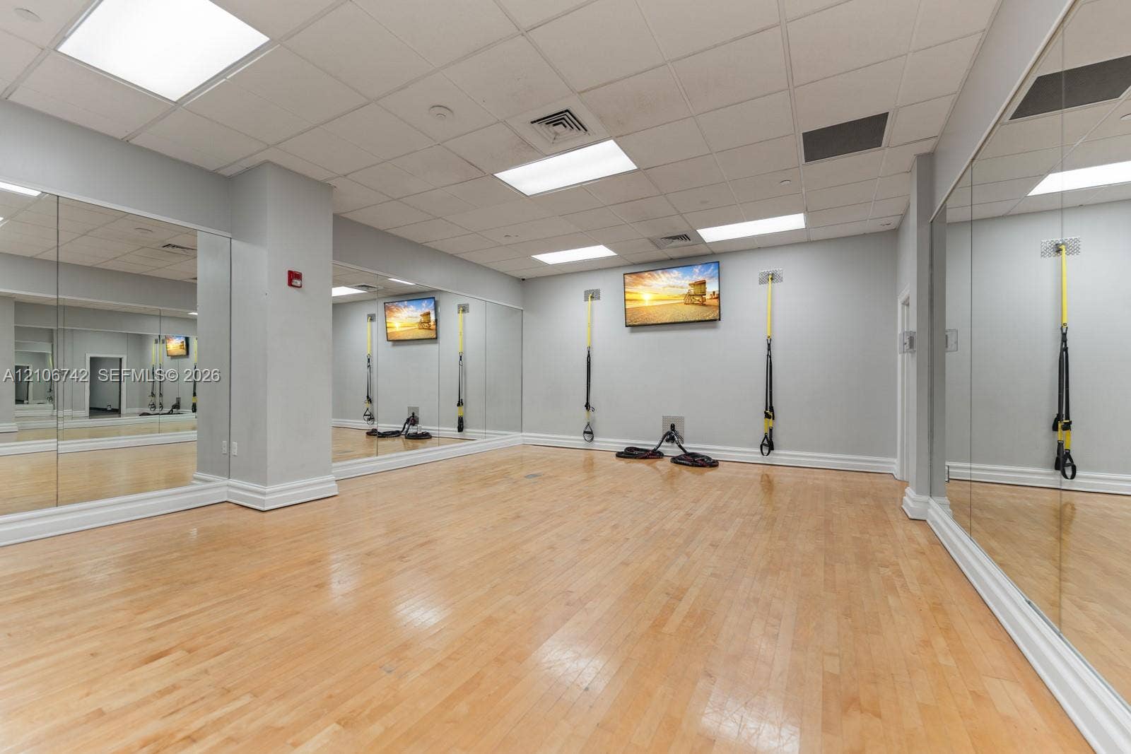 Dedicated fitness space featuring wood-finish flooring, full-length wall mirrors, recessed ceiling lighting, and wall-mounted suspension training equipment