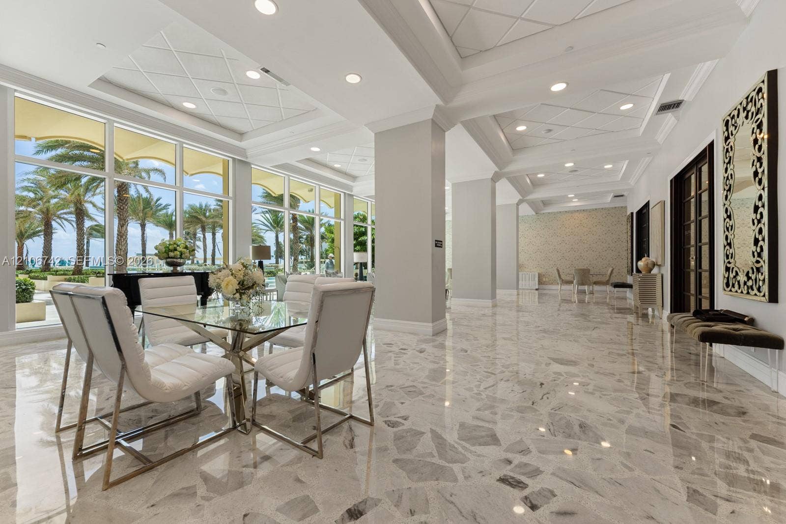 Expansive space featuring polished stone flooring, intricate coffered tray ceilings with recessed lighting, and floor-to-ceiling windows
