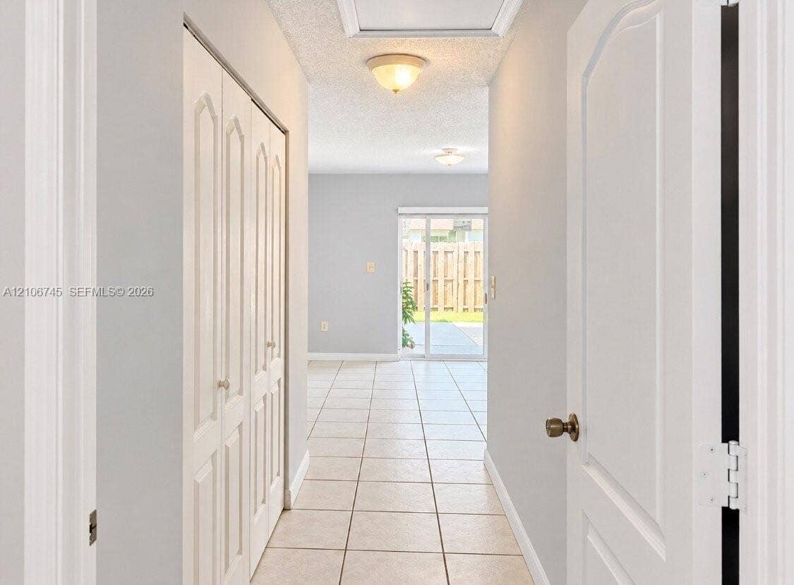 14658 SW 126th Place, Miami, FL 33186 Hallway featuring neutral-toned tile flooring, bi-fold closet doors, and sliding glass exterior doors