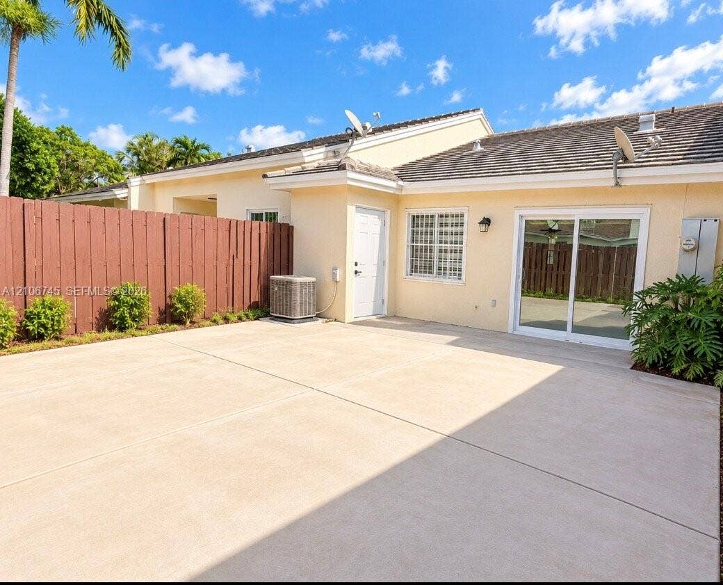 14658 SW 126th Place, Miami, FL 33186 Stucco exterior featuring a concrete patio, tall perimeter wood fencing, sliding glass doors, and a tiled roof