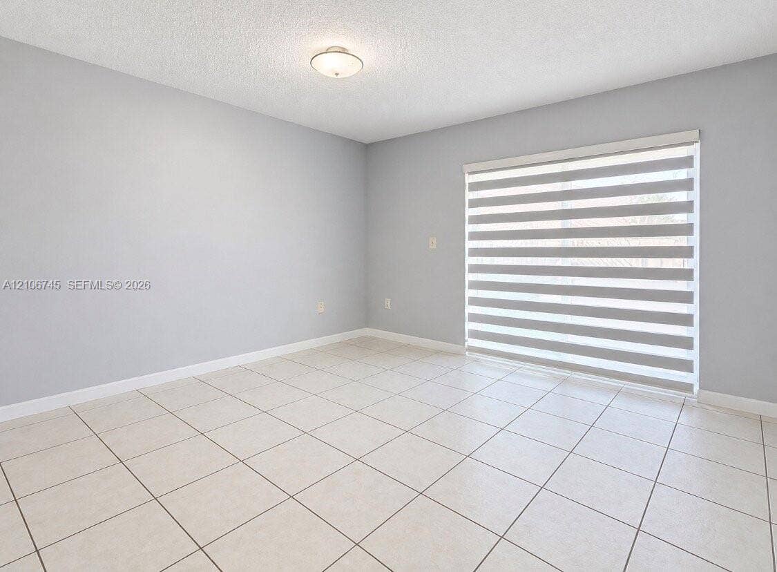 14658 SW 126th Place, Miami, FL 33186 Neutral-toned interior featuring large-format ceramic tile flooring, sliding glass door with horizontal-banded roller shades, and flush-mount ceiling lighting