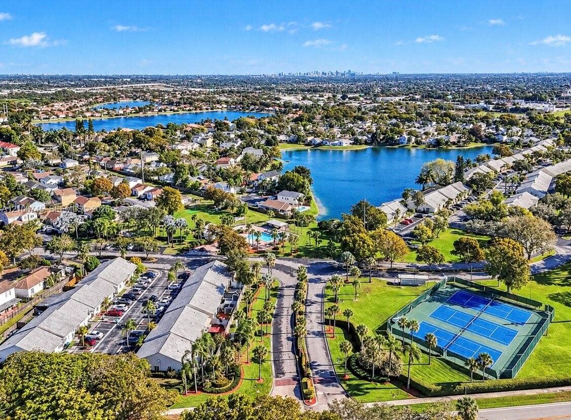 14658 SW 126th Place, Miami, FL 33186 Aerial perspective of the community featuring an outdoor swimming pool, fenced tennis courts, manicured landscaping, and lakefront surroundings