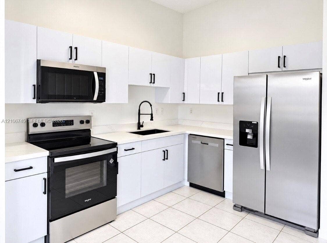 14658 SW 126th Place, Miami, FL 33186 Kitchen featuring white flat-panel cabinetry, stainless steel appliances, solid surface countertops, a matte black high-arch faucet, and tile flooring