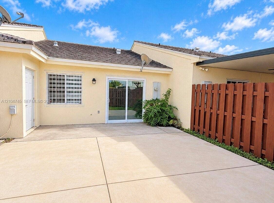 14658 SW 126th Place, Miami, FL 33186 Concrete patio featuring a sliding glass door, exterior wall-mounted lighting, and a wood privacy fence
