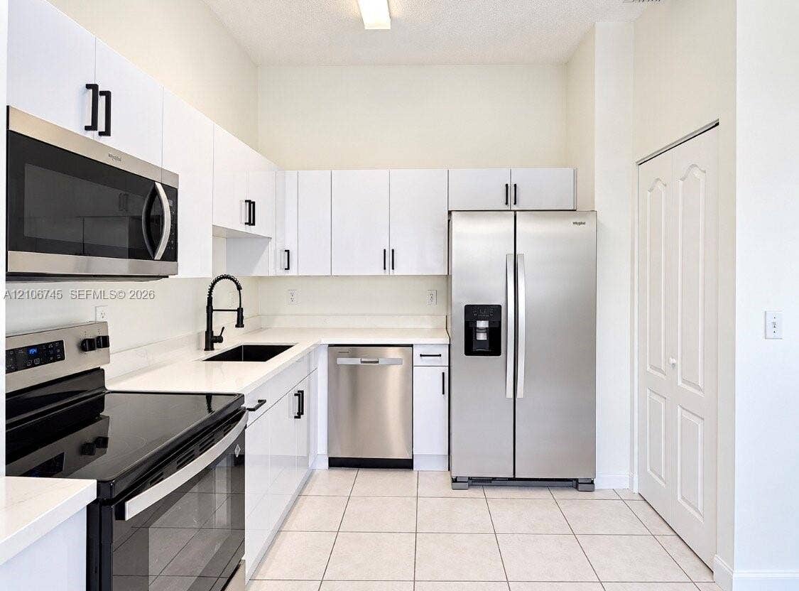 14658 SW 126th Place, Miami, FL 33186 Kitchen featuring white cabinetry, quartz countertops, stainless steel appliances, a black faucet with undermount sink, and tiled flooring