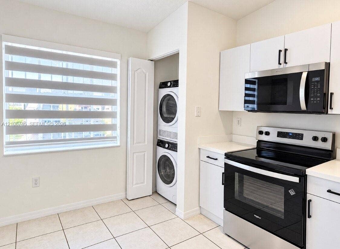 14658 SW 126th Place, Miami, FL 33186 Kitchen featuring white cabinetry, stainless steel appliances, a built-in laundry closet with stacked washer and dryer units, and light-toned tile flooring