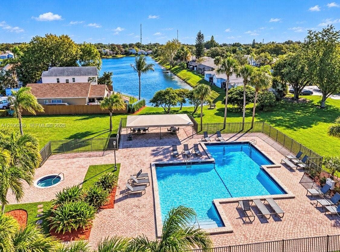 14658 SW 126th Place, Miami, FL 33186 Community swimming pool and spa area featuring paver decking, a covered pavilion, and perimeter fencing, situated along a waterfront lot with mature landscaping