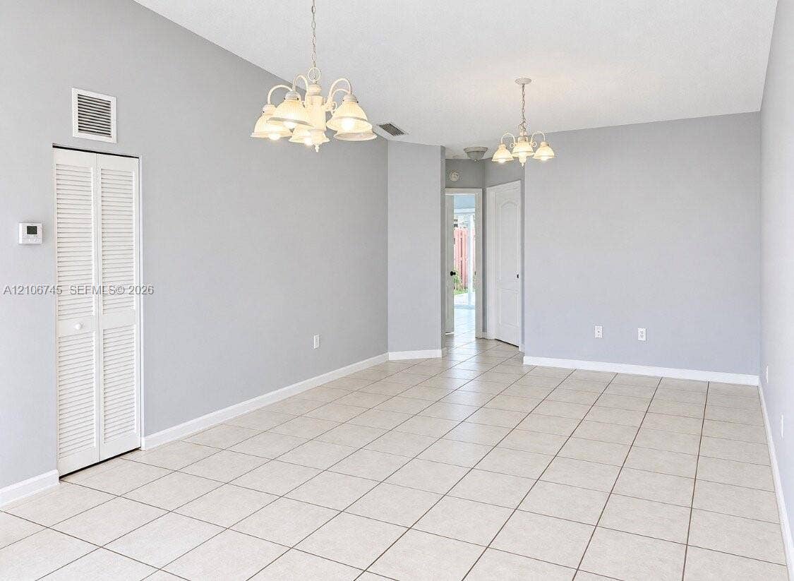 14658 SW 126th Place, Miami, FL 33186 Neutral-toned interior space featuring light-colored tile flooring, dual multi-light chandeliers, and a white louvered-panel closet door