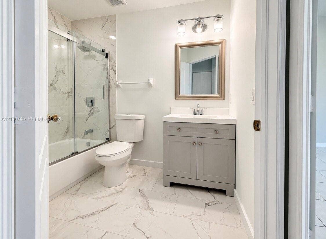 14658 SW 126th Place, Miami, FL 33186 Bathroom featuring large-format veined tile flooring, a grey shaker-style vanity with a solid surface countertop, and a shower-tub combination with sliding glass doors and wall-to-ceiling tile surround