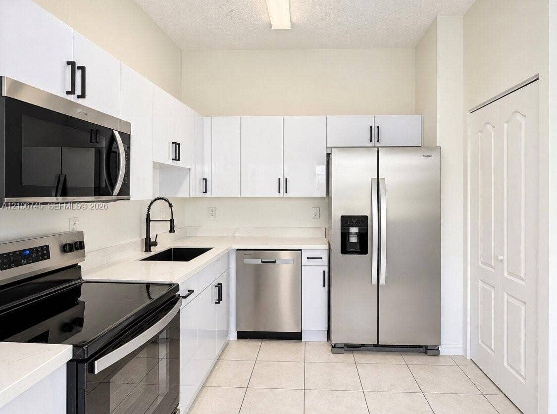 14658 SW 126th Place, Miami, FL 33186 Kitchen featuring white flat-panel cabinetry, light-toned stone countertops, black hardware, stainless steel appliances, and tile flooring