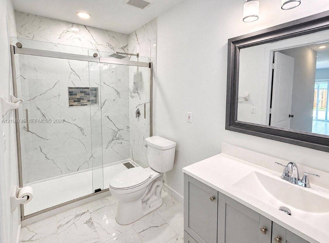 14658 SW 126th Place, Miami, FL 33186 Walk-in shower with floor-to-ceiling stone-patterned tile, glass sliding door, recessed mosaic-tiled niche, gray vanity with white countertop, and framed mirror