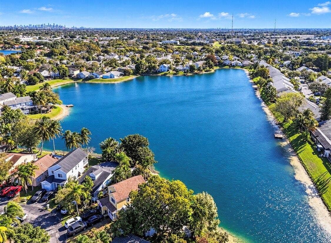 14658 SW 126th Place, Miami, FL 33186 Aerial perspective of a lakefront residential community featuring expansive water frontage, mature tropical landscaping, and clear lines of sight to a distant cityscape skyline