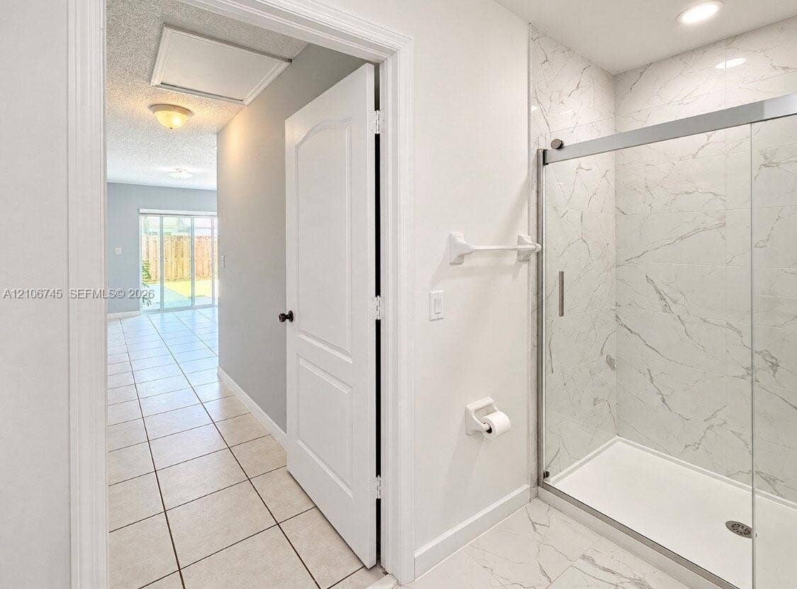 14658 SW 126th Place, Miami, FL 33186 Bathroom featuring a walk-in shower with stone-patterned tile surround, glass sliding enclosure, and light-toned ceramic floor tiling