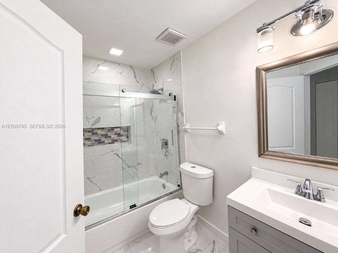 14658 SW 126th Place, Miami, FL 33186 Bathroom featuring a grey vanity with an integrated rectangular sink, stone-patterned tile flooring, a shower-tub combination with glass sliding doors, stone-patterned wall tile, and a recessed decorative tile accent niche