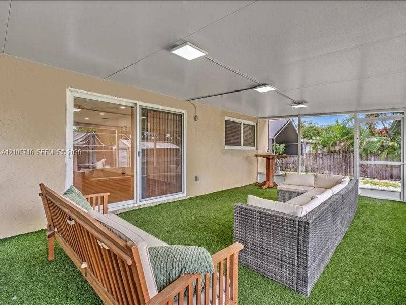 Screened lanai featuring synthetic grass flooring, a solid panel ceiling, surface-mounted square lighting, and dual sliding glass doors