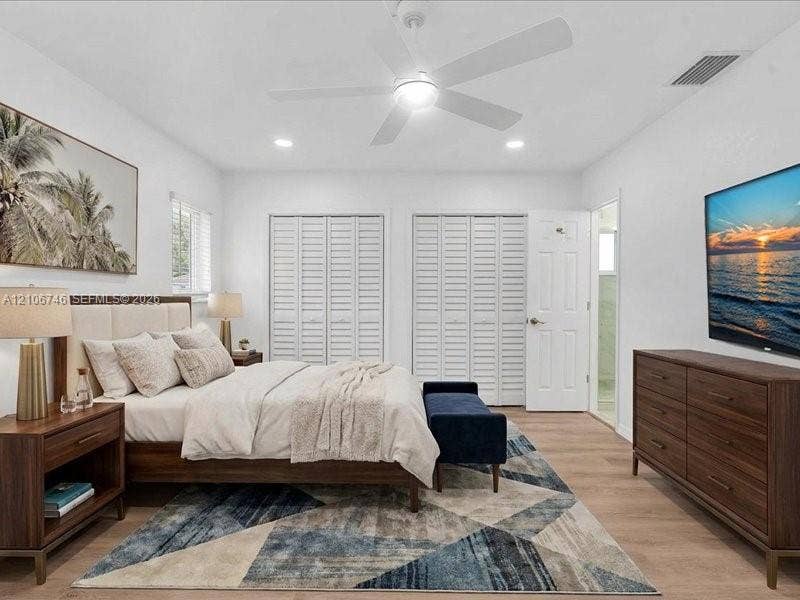 Bedroom featuring wood-finish flooring, dual bi-fold louvered closets, and a white ceiling fan with integrated lighting