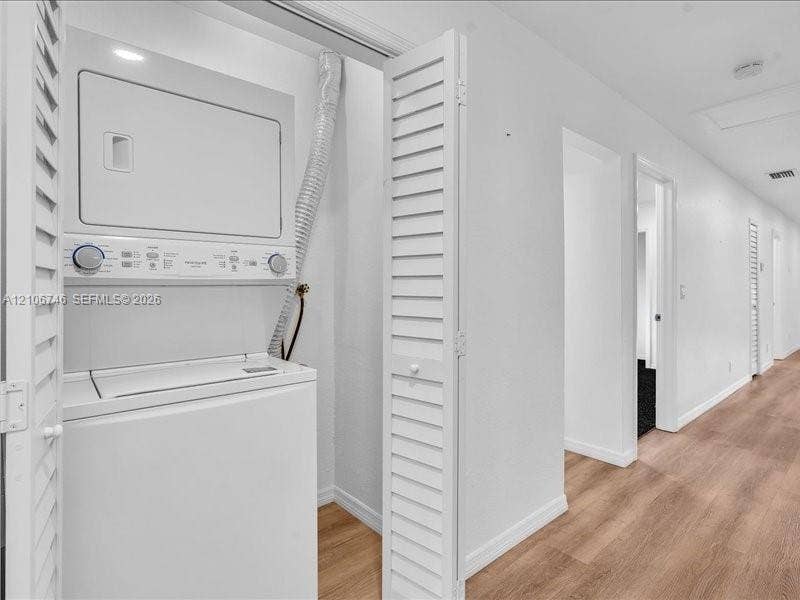 Laundry closet featuring a white stacked washer and dryer unit concealed by bi-fold louvered doors, set against wood-finish flooring