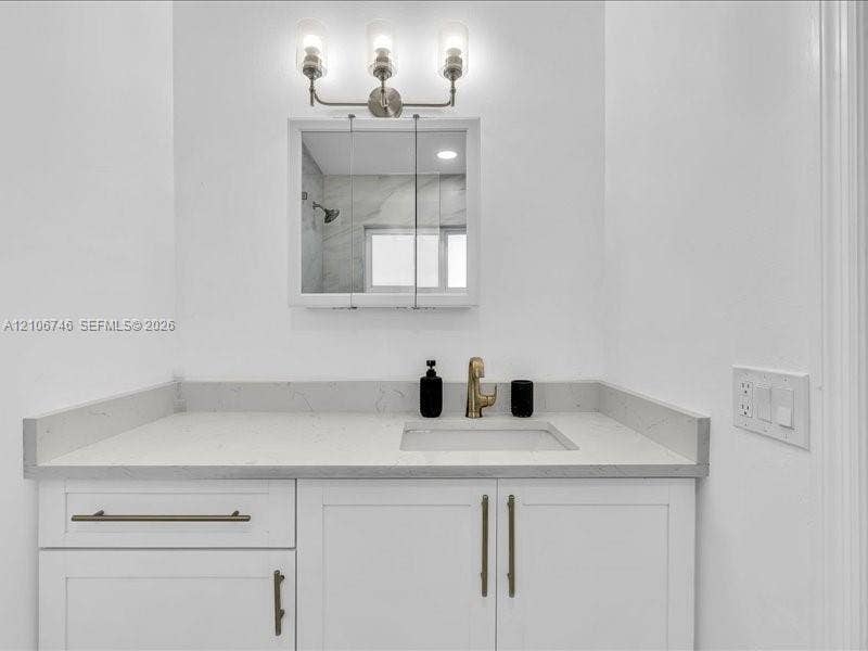 White vanity featuring a solid surface countertop with an integrated basin, brushed metallic faucet, shaker-style cabinetry with elongated hardware, a triple-light wall fixture, and a mirrored medicine cabinet