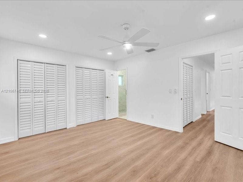 Room featuring wood-finish flooring, dual sets of white louvered-door closets, recessed ceiling lighting, and a white multi-blade ceiling fan