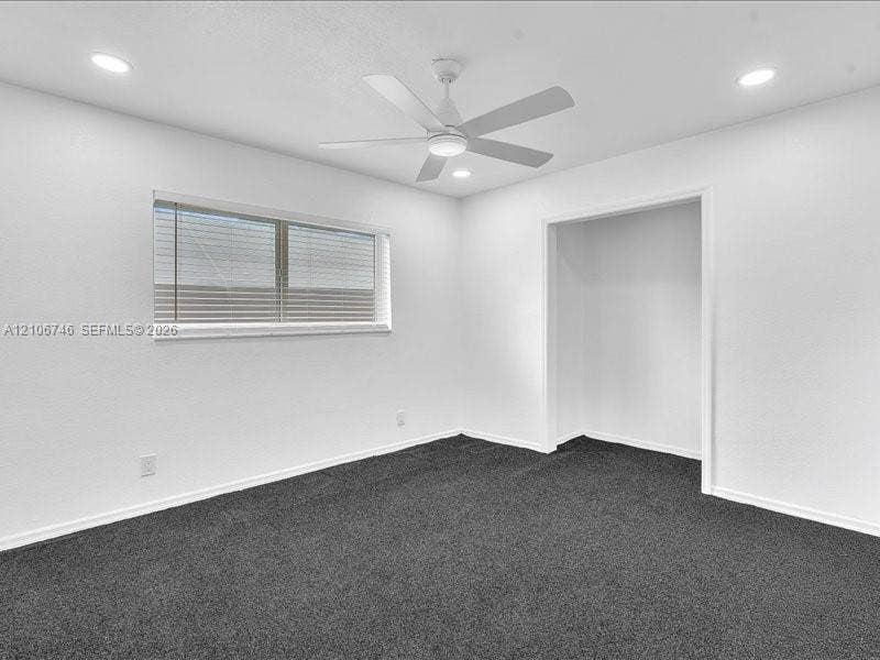Neutral-toned interior space featuring recessed ceiling lighting, a white ceiling fan with integrated light, dark carpeting, and a horizontal window with installed blinds