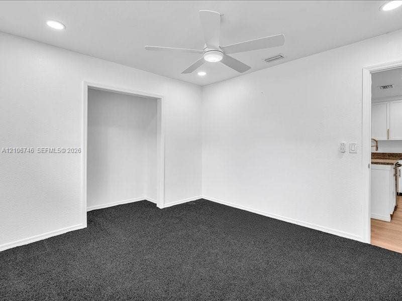Interior room featuring dark carpeting, recessed ceiling lighting, and a white ceiling fan with integrated light