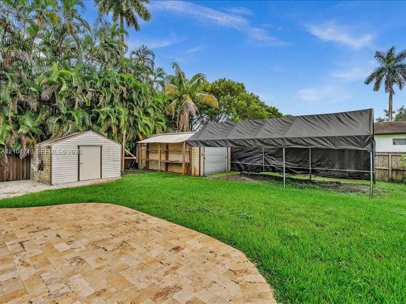 Rear yard featuring a natural stone paver patio, manicured lawn, metal storage shed, and mature palm trees