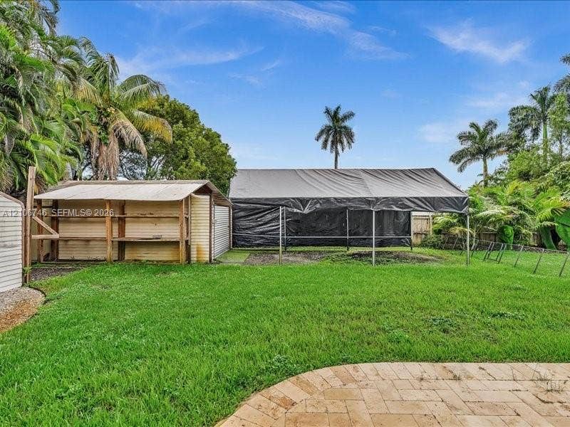 Backyard featuring a grass lawn, paved stone patio, mature palm trees, and two outdoor structures