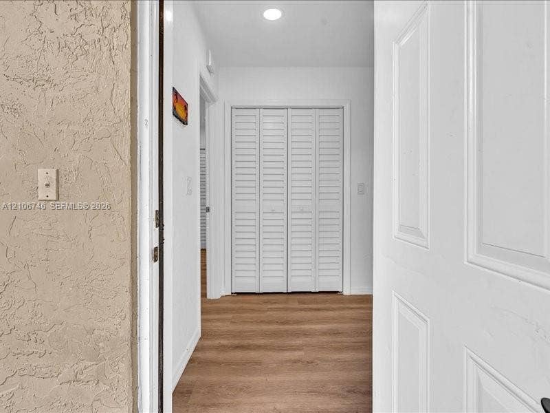 Entryway featuring wood-finish flooring, white paneled doors, and louvered closet doors with recessed ceiling lighting