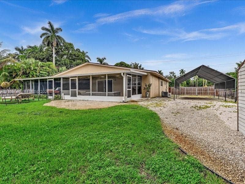 Exterior featuring a screened-in patio, concrete paver patio, metal-frame carport, and perimeter wood fencing