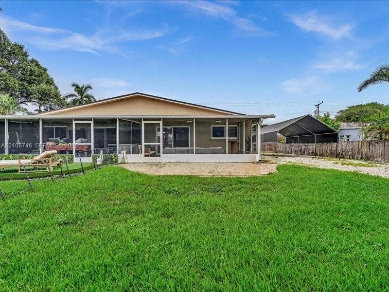 Backyard featuring a screened-in lanai, concrete patio, expansive lawn, metal-roofed carport, and wood privacy fencing