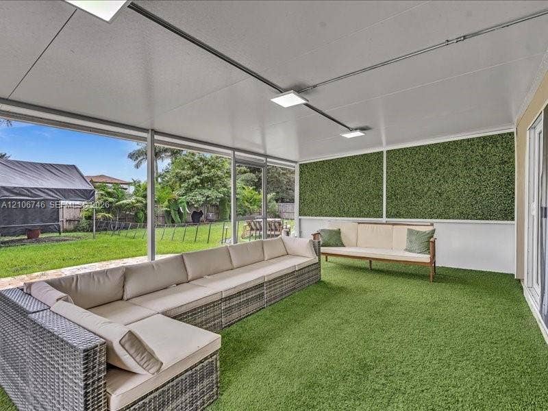 Screened-in patio featuring a solid roof, artificial turf flooring, built-in decorative wall panels, and metal framing
