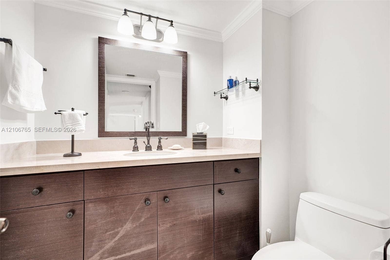 3598 Yacht Club Drive, #901, Aventura, FL 33180 Second bathroom, dark wood-finish cabinetry, light-toned stone countertop, integrated undermount sink, oil-rubbed bronze faucet, three-light vanity fixture, and rectangular framed mirror.