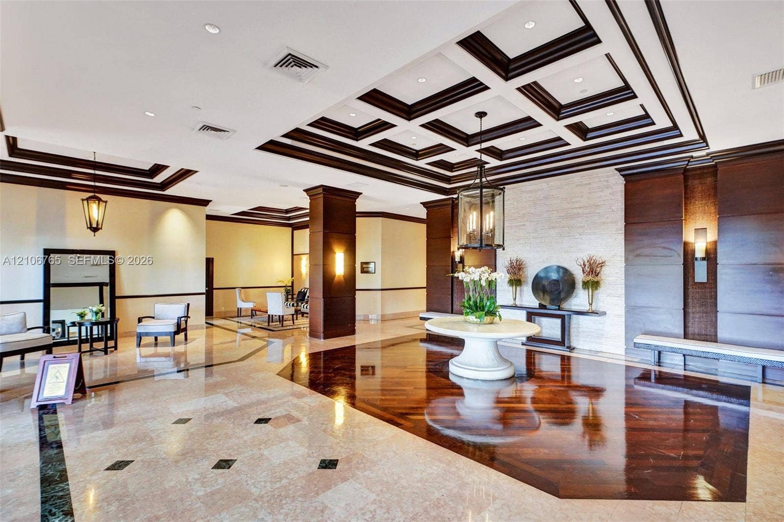 3598 Yacht Club Drive, #901, Aventura, FL 33180 Coffered ceiling with dark wood detailing, inlaid stone flooring, textured stone accent wall, wood-paneled columns, and lantern-style light fixtures.