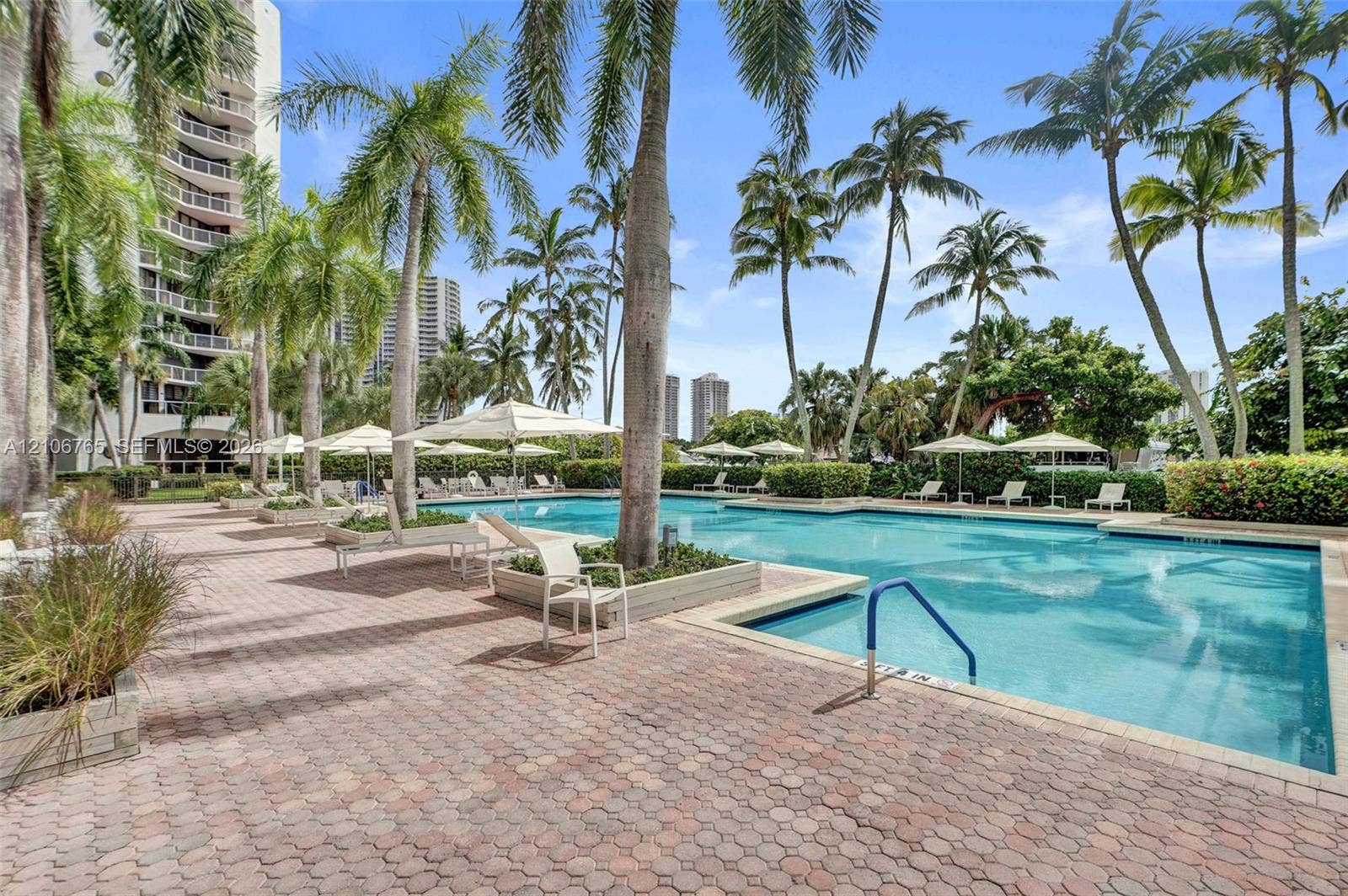 3598 Yacht Club Drive, #901, Aventura, FL 33180 Resort-style swimming pool featuring a brick paver deck, palm tree landscaping, built-in planters, and multi-level water entry